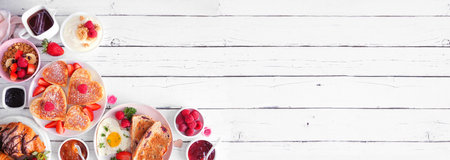 Valentines or Mothers Day brunch corner border. Top down view on a white wood banner background. Heart shaped pancakes, eggs and a variety of love themed food.の写真素材