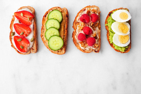 Healthy toast set with assorted proteins and fruits. Above view on a white marble background....