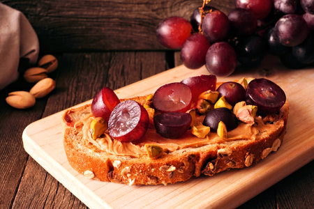 Healthy breakfast toast with nut butter, grapes and pistachios on multi grain bread. Close up on a dark wood background.の写真素材