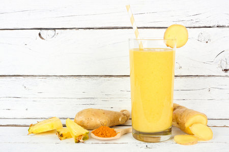 Pineapple, turmeric and ginger smoothie against a white wood background with ingredients. Healthy immune boosting, weight loss, anti-inflammatory.の写真素材