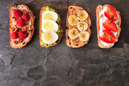 Healthy toast set with a variety of proteins and fruits. Top view on a dark background with copy space. Cream cheese nut raspberry, avocado egg, peanut butter banana chia, strawberry yogurt.の写真素材