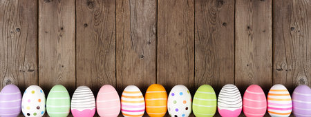 Colorful Easter Egg long bottom border. Top down view against a rustic wood banner background. Copy space.の写真素材