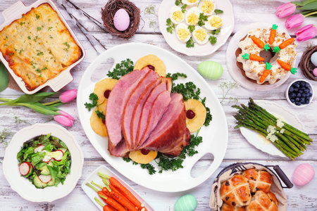 Traditional Easter ham dinner. Top view table scene on a white wood background. Ham, scalloped...