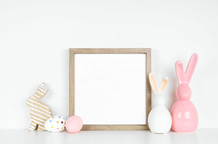 Mock up wood frame with Easter egg and bunny decor on a white shelf. Square frame against a white...