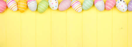 Colorful Easter Egg top border over a soft yellow wood banner background. Overhead view with copy space.の写真素材