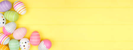 Colorful Easter Egg corner border over a soft yellow wood banner background. Above view with copy space.の写真素材