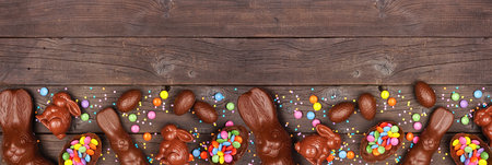 Easter candy and chocolate bunnies and eggs. Bottom border against a rustic dark wood banner...