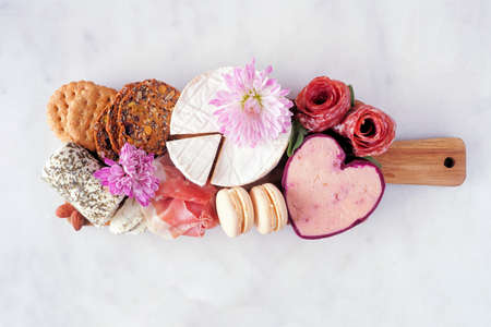 Mother's Day theme charcuterie board against a white marble background. Variety of cheese, meat, fruit and sweet appetizers. Overhead view.の写真素材
