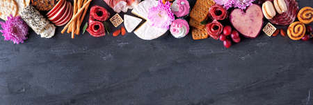 Mother's Day charcuterie top border against a dark slate banner background. Assortment of cheese, meat, fruit and sweet appetizers. Copy space.の写真素材