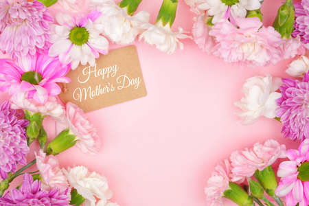 Happy Mothers Day gift tag with frame of pink and white flowers. Top view on a pink background. Copy space.の写真素材