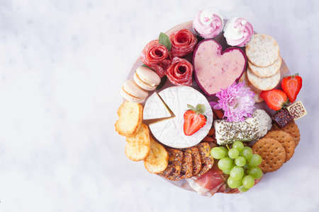 Mother's Day theme charcuterie board against a white marble background. Assortment of cheese, meat, fruit and sweet appetizers. Top down view.の写真素材