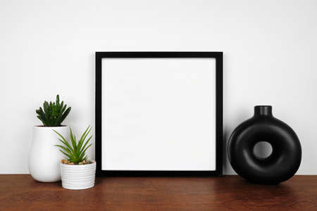 Mock up black square frame with succulent plants and modern circle vase. Wooden shelf against a white wall. Copy space.の写真素材
