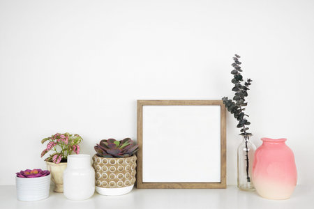 Mock up wood square frame with pink hue decor. White shelf against a white wall. Copy space.