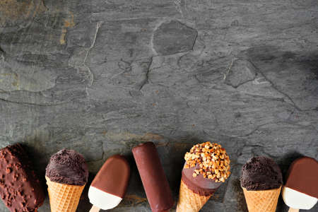 Assortment of chocolate ice cream desserts. Top view bottom border over a dark slate background with copy space.の写真素材