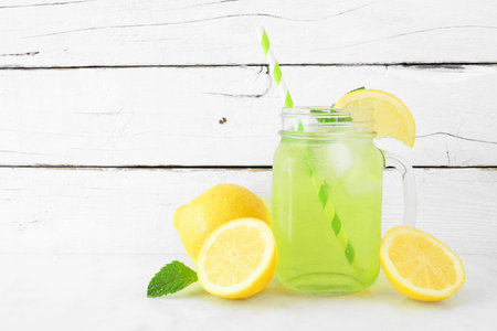 Iced herbal green tea in a mason jar glass with paper straw against a white wood background