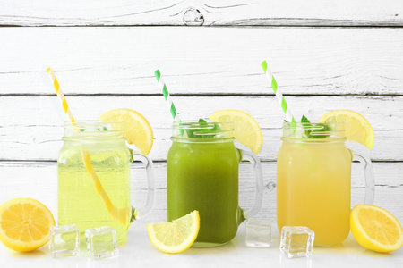 Set of summer iced green teas in mason jar glasses with paper straws against a white wood background. Iced green tea, iced matcha lemonade and iced green tea lemonade.の写真素材