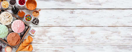 Summer ice cream bar with assorted ice cream flavors and delicious toppings. Above view side border over a rustic white wood banner background.の写真素材