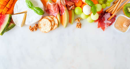 Summer fruit theme charcuterie top border against a white marble background. Mixture of fruits, cheese and meat appetizers. Copy space.の写真素材