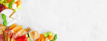 Summer fruit theme charcuterie corner border against a white marble background. Selection of fruits, cheese and meat appetizers. Copy space.の写真素材