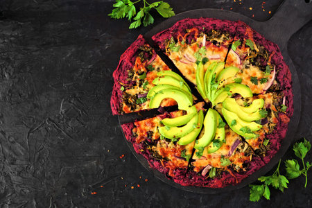 Healthy, low carb beet crust pizza with avocados, pesto sauce and onions. Above view with cut slices on a dark slate background.の写真素材