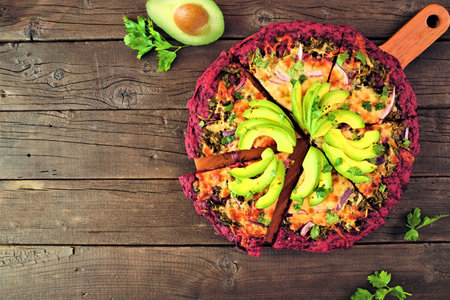 Healthy, gluten free beet crust pizza with avocados, pesto sauce and onions. Top view with cut...