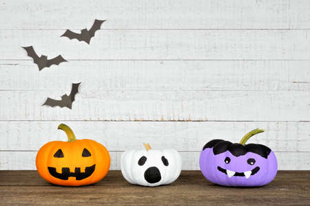 Painted Halloween pumpkins on a wood shelf against a rustic white wood background with bats. Jack o Lantern, ghost and vampire.の写真素材