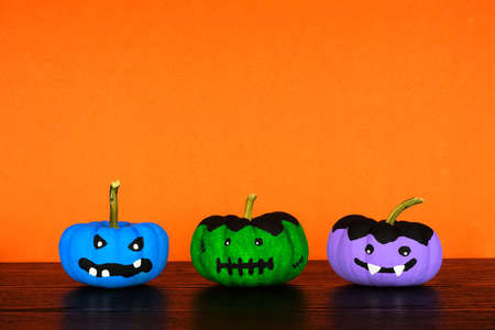 Painted Halloween pumpkins on a black shelf against an orange background. Monster, frankenstein and vampire.の写真素材