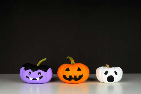 Painted Halloween pumpkins on a white shelf against a black background. Monster, Jack o Lantern and ghost.の写真素材