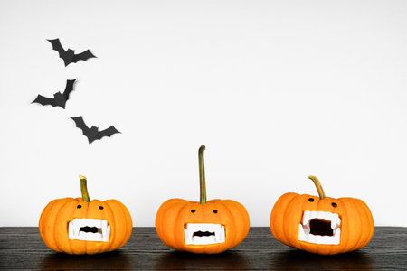 Fun Halloween pumpkins with vampire teeth on a black shelf against a white wall with bats. Copy space.の写真素材