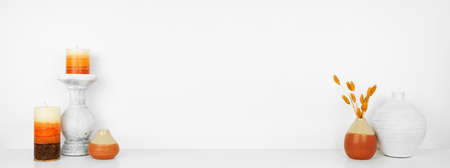 Fall decor on a white shelf against a white wall background. Banner with copy space. Candles, vases and vibrant branches.の写真素材