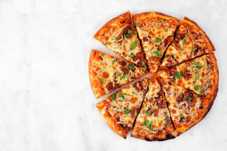 Autumn pizza with pumpkin sauce, gouda and caramelized onions. Sliced. Above view on a white marble background.の写真素材