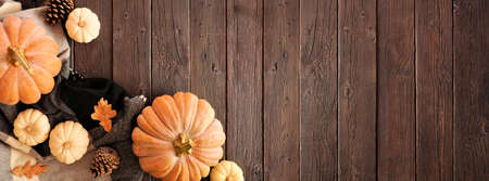 Cozy autumn corner border on a rustic dark wood banner background. Top view. Blanket, pumpkins and natural decor. Copy space.の写真素材