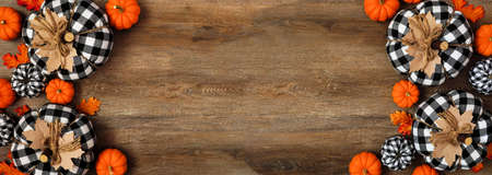 Autumn double border of leaves, orange, and black and white buffalo plaid pumpkins over a wood banner background. Top view with copy space.の写真素材