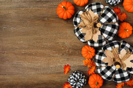 Autumn side border of leaves, orange, and black and white buffalo plaid pumpkins over a wood background. Overhead view with copy space.の写真素材