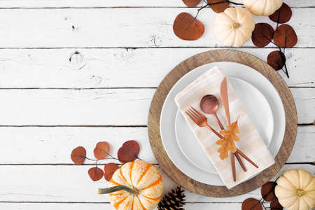 Autumn harvest or thanksgiving dinner table setting with plates, flatware, napkin and fall decor. Overhead view corner border on a white wood background with copy space.の写真素材