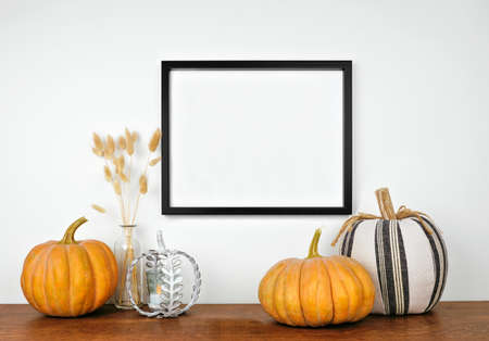 Mock up black frame hanging from a white wall with pumpkins and fall decor on a wood shelf. Autumn concept. Copy space.の写真素材