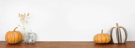 Fall decor on a wood shelf against a white wall banner background. Rustic pumpkins, candle and branches. Copy space.の写真素材