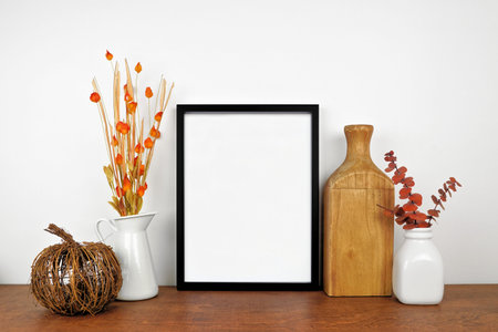 Mock up black frame with autumn branches and decor on a wood shelf. Fall concept. Portrait frame...