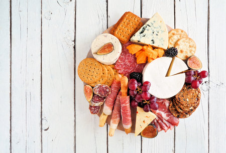 Charcuterie platter with different meats, cheeses and appetizers. Top view on a white wood background.の写真素材