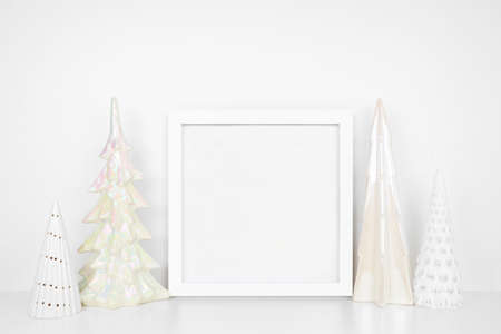 Christmas mock up with white frame and shiny glass tree decor. Square frame on a white shelf against a white wall. Copy space.の写真素材