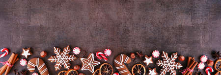 Christmas baking bottom border with cookies, peppermints and spices. Top down view on a dark stone background with copy space. Holiday baking concept.の写真素材