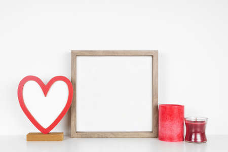 Mock up square wood frame with Valentines Day blank heart sign and candles. White shelf against a white wall. Copy space.の写真素材