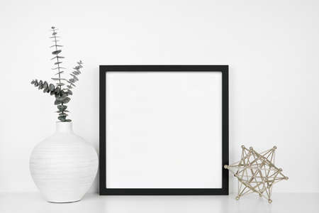 Mock up black square frame with modern home decor. White shelf against a white wall.  Eucalyptus branches in vase with geometric table top decoration. Copy space.の写真素材