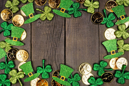 St Patricks Day frame against a dark wood background. Top down view with gold coins, shamrocks and...