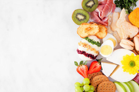 Spring or Easter charcuterie corner border against a white marble banner background. Top down view. Variety of cheese, meat and fruit appetizers. Copy space.の写真素材