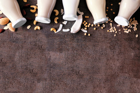 Vegan plant based nondairy milk corner border. Variety in milk bottles with scattered ingredients. Top view over a brown stone background with copy space.の写真素材