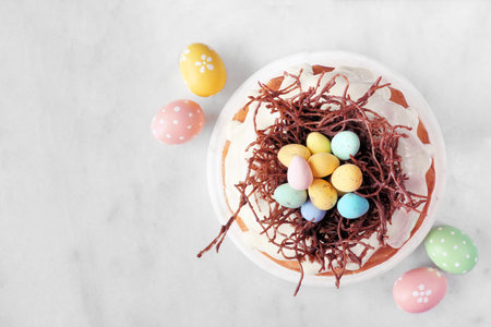 Easter bundt cake with chocolate nest of colorful candy eggs. Overhead view on a white marble...