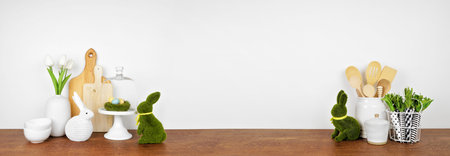 Easter theme kitchenware, utensils and decor on a wood shelf or counter. Banner against a white wall...
