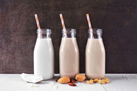 Vegan, plant based, non dairy milk. Coconut, almond and cashew in milk bottles with scattered...