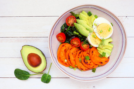 Breakfast nutrient bowl with sweet potato, egg, avocado and spinach. Top view table scene on a white...